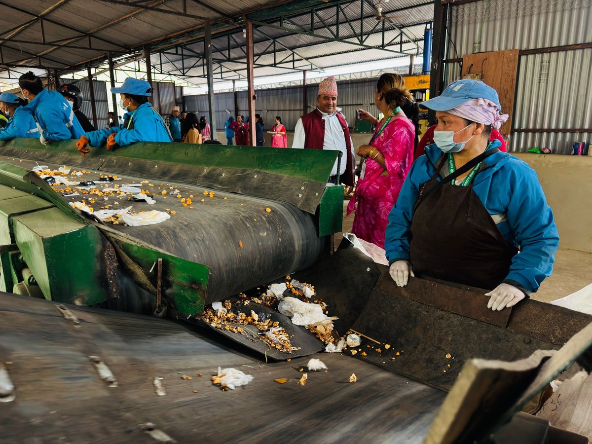 Workers at a materials recovery facility sorting mixed household recyclables on a conveyor belt.