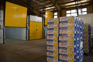 Stacks of banana boxes in a modern industrial cold storage warehouse with large yellow temperature-controlled doors.
